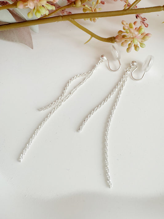 Silver chain clip on earrings on a light background with floral elements