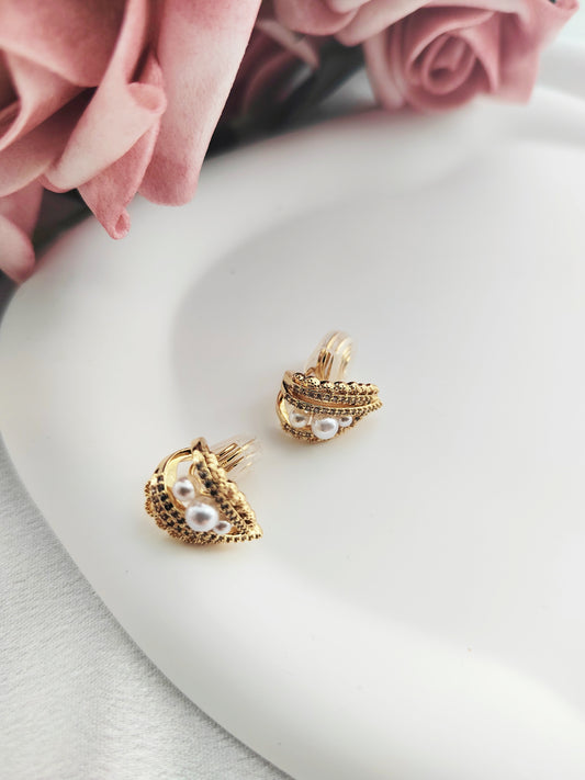 Gold clip on earrings with pearl accents on a white plate with pink roses.
