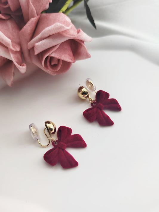 Red bow clip on earrings with gold accents on a white surface with pink roses.